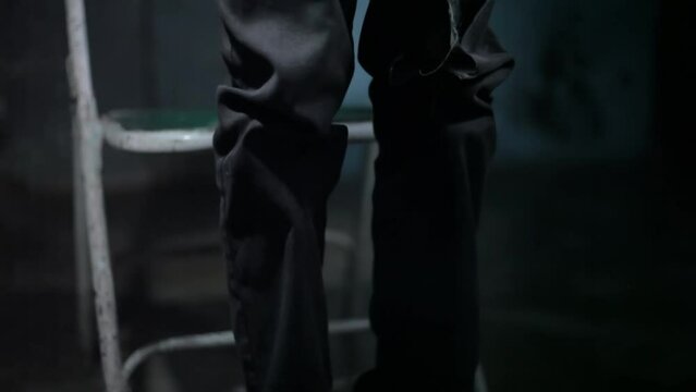 Detained man with torn clothes standing up by kicking a stool in a dark room, 24 fps footage in HD.
