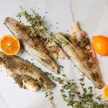 sea bass fillet with herb marinade, lemons and thyme on a light table