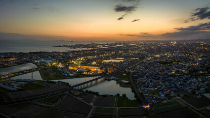 Train tracks over pond with sunset glow in sky as city lights up at dusk