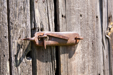 An old, original doorknob on a centuries-old wooden barn door in the harsh afternoon sun. Day.