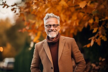 Portrait of a happy senior man in a coat and glasses standing in the autumn park.