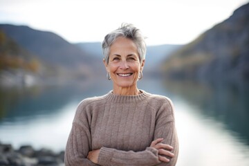 Fototapeta na wymiar Medium shot portrait photography of a pleased woman in her 50s that is wearing a cozy sweater against a mountain lake or alpine background . Generative AI