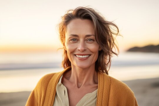 Portrait of smiling mature woman in sweater standing on beach at sunset
