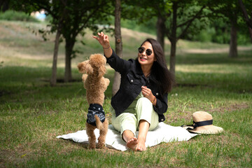 An Asian girl (Kazakh woman) feeds her dog (mini poodle) from her hands. Summer portrait of a young...