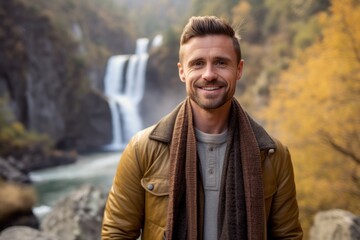 Portrait of a handsome man standing in front of a waterfall in autumn