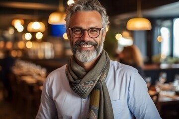 Fototapeta premium Portrait of smiling mature man wearing eyeglasses and scarf in restaurant