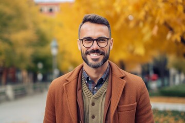 Portrait of handsome bearded man wearing coat and eyeglasses standing in the autumn street.