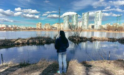 Fototapeta premium A woman stands on the shore of the lake and looks at the city on the other side