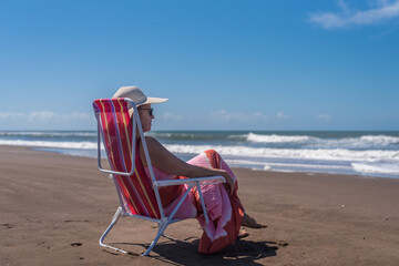 Mature woman relaxing sitting on a beach chair at the beach. Summer concept.