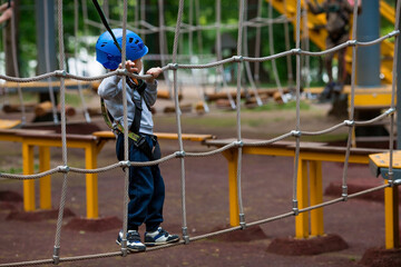 Summer. A small child climbs in a rope park on a rope bridge. A boy is having fun in an Adventure Park. A male baby on a climbing frame. Compliance with safety techniques.