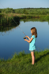 Seven year old girl fishing on the summer lake with a fishing rod