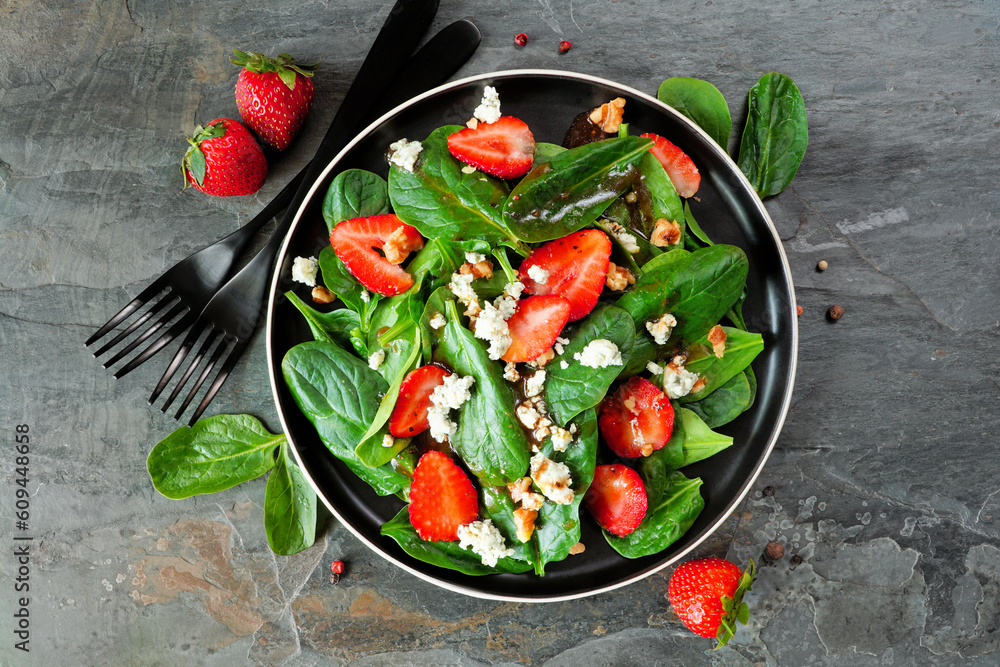 Poster Summer salad of spinach, strawberries and blue cheese in a black plate. Above view with ingredient frame on a dark slate background.