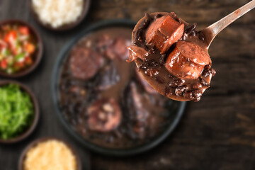 Selective focus on spoon with Brazilian Feijoada Food. Traditional Brazilian food made with black...