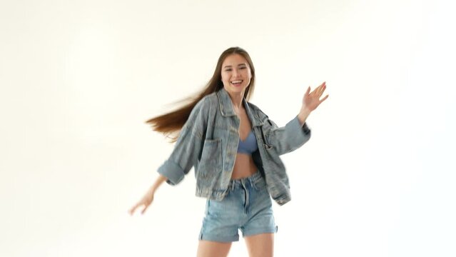 Young Asian woman dancing on white background. She has long hair and wearing short denim shorts and a denim jacket. Joyful girl enjoying her favorite music.