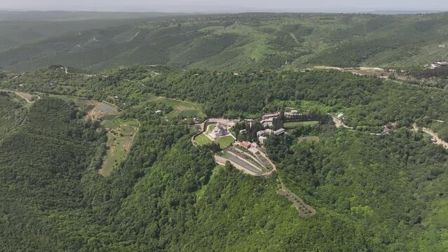Aerial view of monastic complex of Bodbe nunnery on hillside among tall Cypress trees with Church of St. Nino on sunny day, Sighnaghi, Georgia