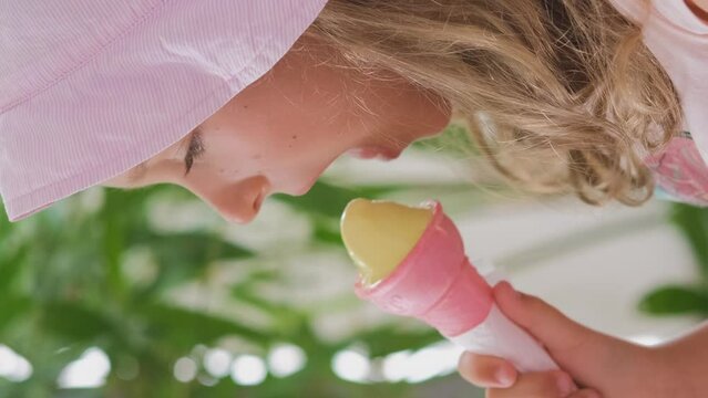 Vertical video. Happy little girl eating ice cream in pink crispy cone in summer day, slow motion