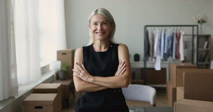 Cheerful confident property buyer woman posing with cardboard relocation boxes in new apartment, looking at camera with happy smile and arms folded, smiling. Home owner portrait