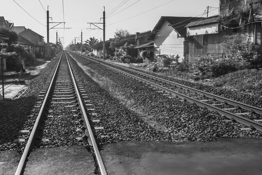 Perspective photo of Classic Railroad Train tracks with gravels, small stones, pebble rocks, and asphalt road. Bright Sunny Daylight during the day with blue sky background.