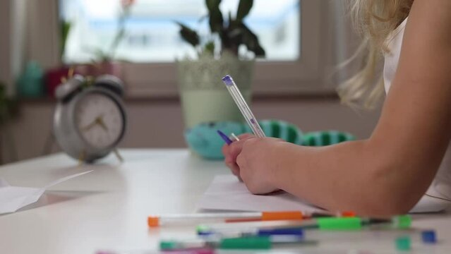 Child girl draws with her left hand sitting at the table