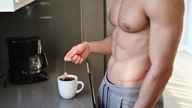 Shirtless muscular handsome guy brewing tea in morning