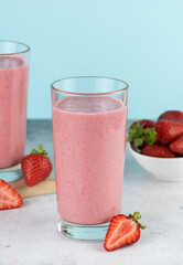 Strawberry smoothie or milkshake with berries on a blue background. Summer beverages.
