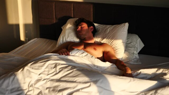 Handsome shirtless young man in bed sleeping and waking up