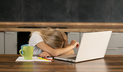 Tired girl rested her head on the table next to the laptop, sitting at the kitchen table in the apartment. Distance work of stulent or businesswoman. Difficult preparation for exams