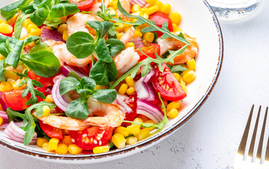 Fresh tasty salad with shrimps, sweet corn, avocado, red cherry tomatoes, lamb lettuce and onion on white table background. Top view