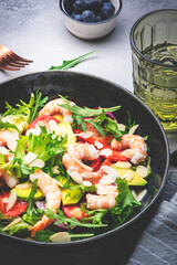 Strawberry, shrimp and herbs salad with arugula, lettuce, avocado and almond slices, gray table. Fresh useful dish for healthy eating. Top view