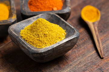 Turmeric, pepper and curry powder in container on wooden background