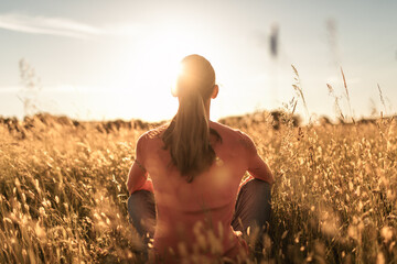 Young female sitting in wheat field feeling grateful, joyful outdoors in the sunrise	