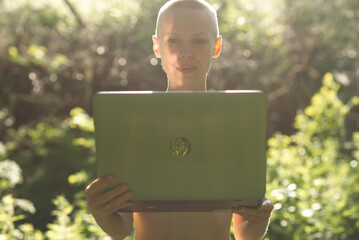 woman with a shaved head without makeup in nature with a laptop