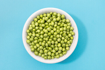 Fresh green peas in bowl isolated on blue background. Top view