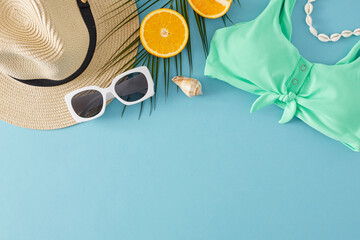 The idea of a beachfront summer respite. Top view flat lay of sun hat, sunglasses, shell choker necklace, orange, palm leaf, seashell on light blue background with empty space for promo or text
