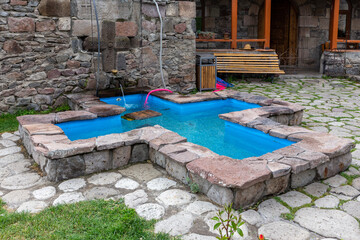 Cross-shaped stone pool with turquoise clear water in Zarzma Monastery of Transfiguration, medieval Orthodox Christian monastery located in the village of Zarzma, Georgia.