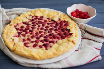 Homemade raspberry cake or galette on blue wooden table over a white cloth, with fresh berries on side, side view.