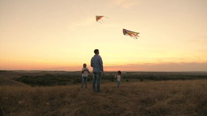 Fototapeta na wymiar Dad and beloved daughters launch colorful paper planes into the sky. dad with children playing with kites at sunset in the park. healthy family outdoors. fun to play with parents in the sun