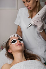 beautician holding beauty laser near woman face,protective eyewear, spa procedures with laser and...