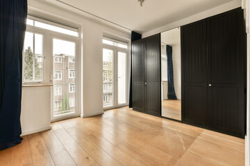 an empty room with wood flooring and black closets on either side of the room, looking out onto the street
