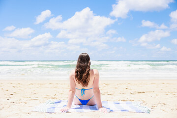 水着でビーチに座るオーストラリア少女の後ろ姿