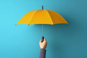 Fotobehang Hand holding yellow umbrella on blue background, Generative AI © Kaleb