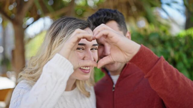 Man and woman couple smiling confident doing heart gesture with hands at park