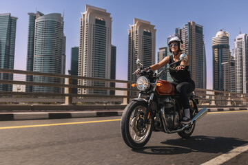 Fototapeta na wymiar woman driving a classic motorbike excited on a dubai downtown road skyscrapers in the background