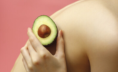 woman with avocado in hand near body isolated on pink background