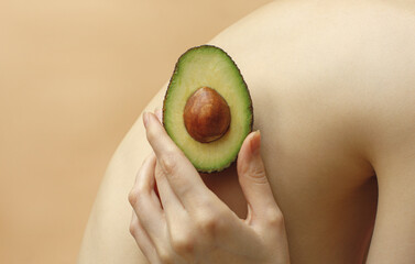 woman holding a avocado near her skin on back, isolated on beige background