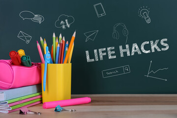 Words Life Hacks and drawings on green chalkboard near wooden table with stationery © New Africa