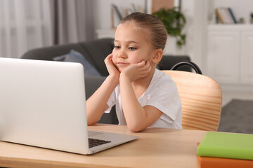 Little girl using laptop at table indoors. Internet addiction