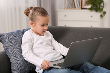 Little girl using laptop on sofa at home. Internet addiction