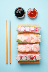 Different delicious spring rolls, chopsticks and sauces on light blue background, flat lay