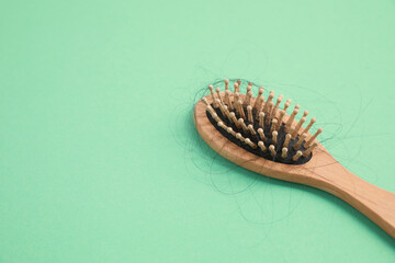 Wooden brush with lost hair on green background, closeup. Space for text